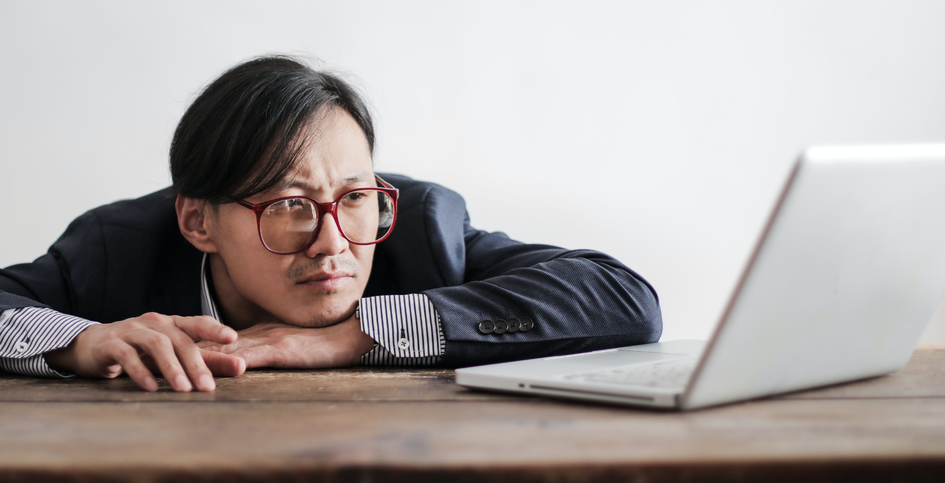 A person rests their head on their hand while staring at a laptop on a table